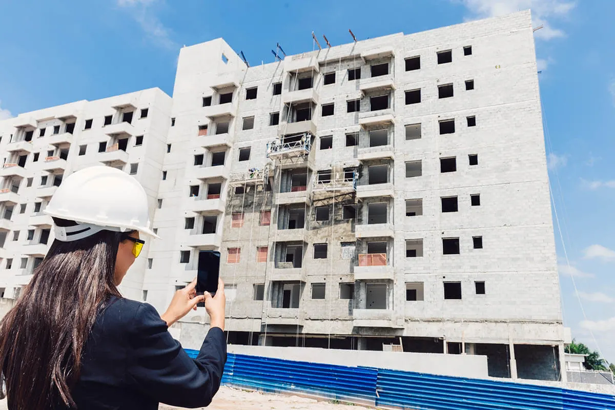 Site manager in a white hard hat photographing a new apartment building