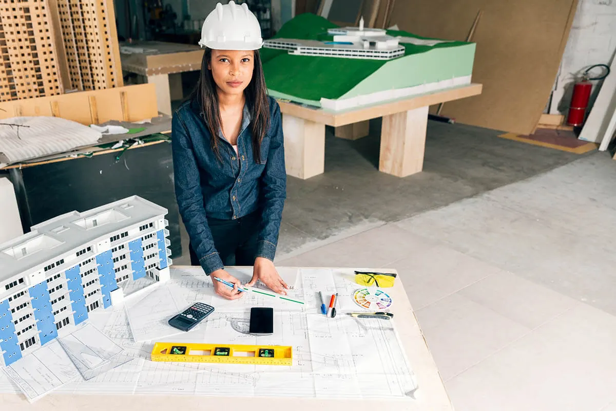 Site manager in a hard hat reviewing plans beside a scale model of a development