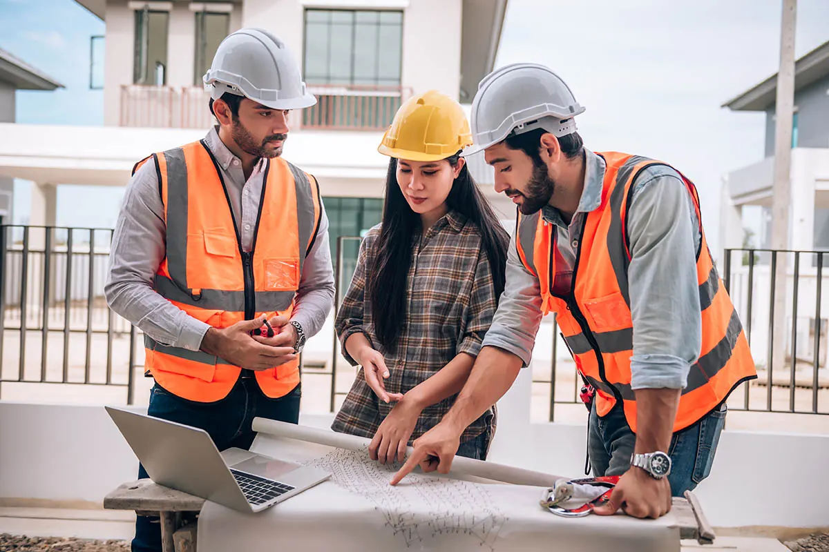 Three construction professionals reviewing building plans on site