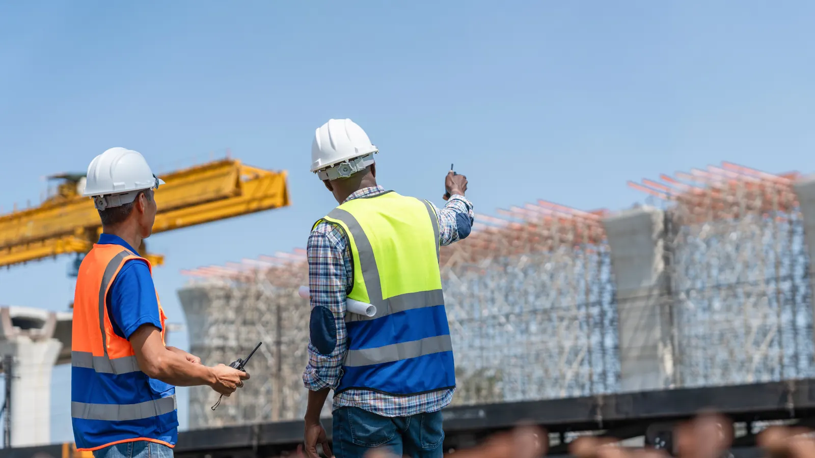 Two construction workers in hard hats and hi-vis vests looking at a site beside a crane