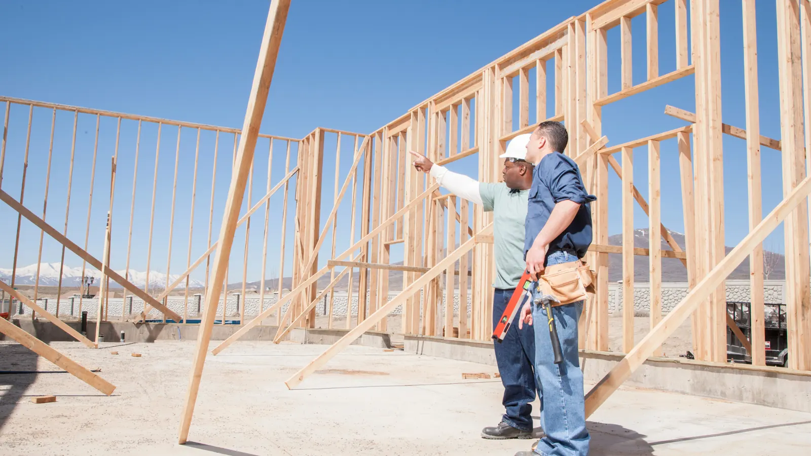 Two builders working beside a timber stud frame on a building site