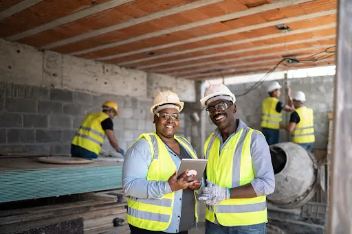 Two builders in hard hats and hi-vis jackets reviewing a tablet inside a building shell