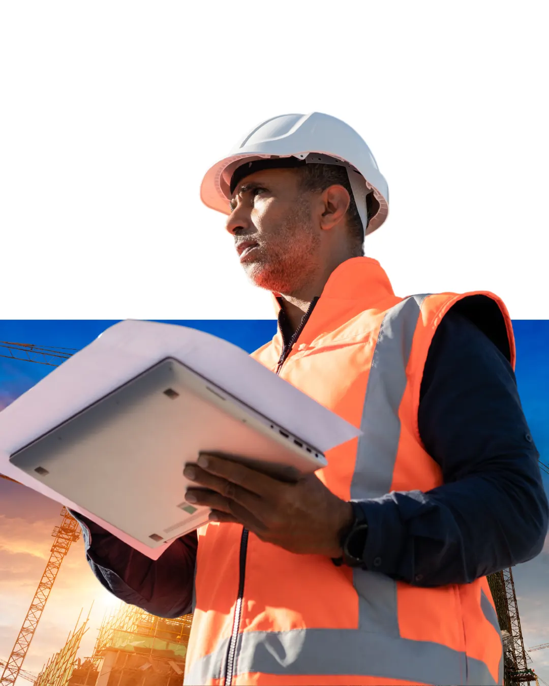 Construction worker in a hard hat and hi-vis vest holding a tablet at sunset