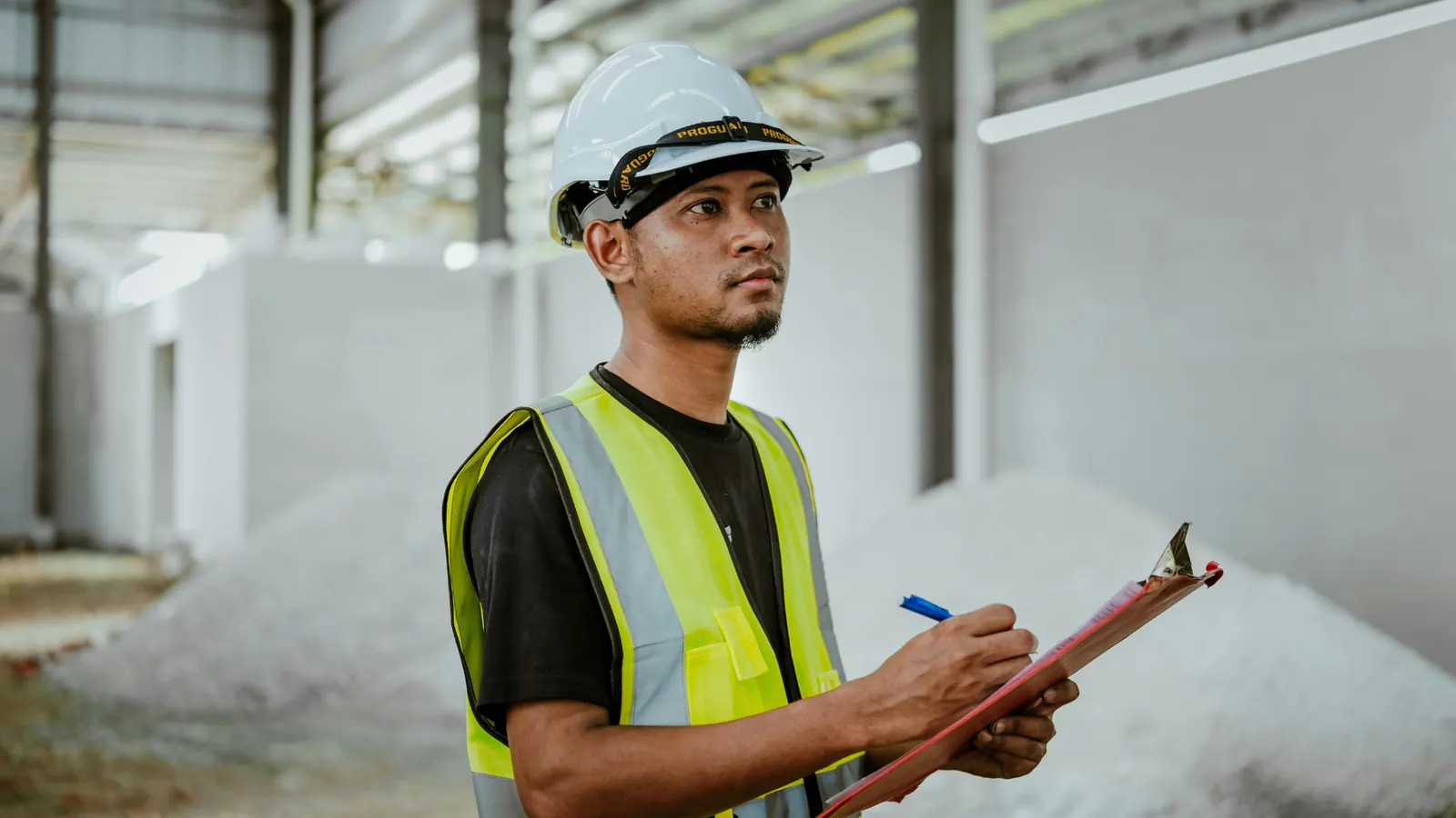 Site worker in hard hat and hi-vis vest making notes on a clipboard inside a building shell